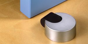 Tope de puerta adhesivo Inofix 2021 con amortiguador negro, instalado sobre suelo de madera clara para evitar golpes de puertas y proteger superficies