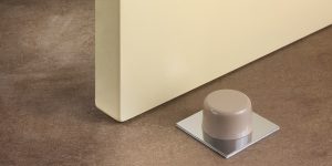 Tope de puerta adhesivo Inofix 2023 con base metálica, instalado sobre suelo liso, ideal para proteger paredes del impacto de puertas interiores