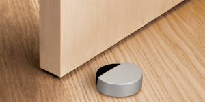 Tope de puerta adhesivo Inofix 2027 color plata con espuma amortiguadora, instalado sobre suelo de madera para proteger la pared del impacto de la puerta