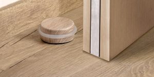 Tope de puerta Inofix 2098 con acabado laminado efecto madera instalado sobre suelo de parquet, con anillo de silicona amortiguador para evitar golpes en puertas interiores
