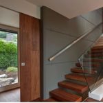 Puerta corredera empotrada en cart&oacute;n yeso con sistema Mekkit3D Krona, estructura oculta y acabado en madera, integrada en interior moderno con escalera de dise&ntilde;o