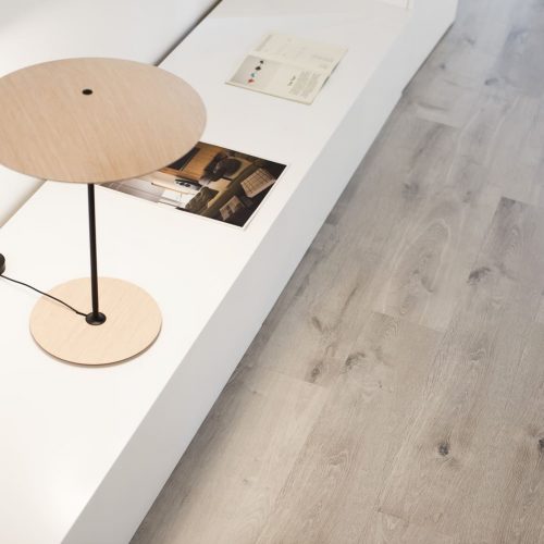 Suelo laminado de resina Flint HI FLOOR AC6 instalado en baño moderno, con acabado efecto piedra gris clara, resistente a la humedad y de alta durabilidad.