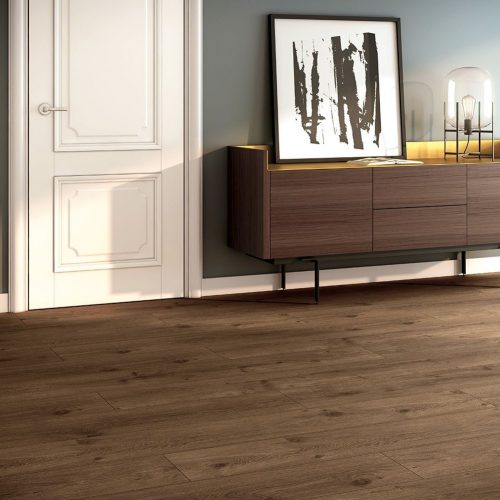 Suelo laminado Finfloor XL AC6 Durable PRO en salón moderno, acabado roble oscuro con lamas extragrandes, alta resistencia al desgaste y al agua, ideal para espacios elegantes y de uso intensivo.