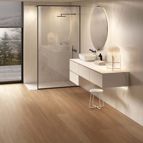 Baño moderno con ducha de vidrio y mueble suspendido, donde destaca el suelo laminado Flint Connect AC5 en tono roble cálido, con lamas largas y vetas naturales que aportan continuidad, elegancia y sensación acogedora.